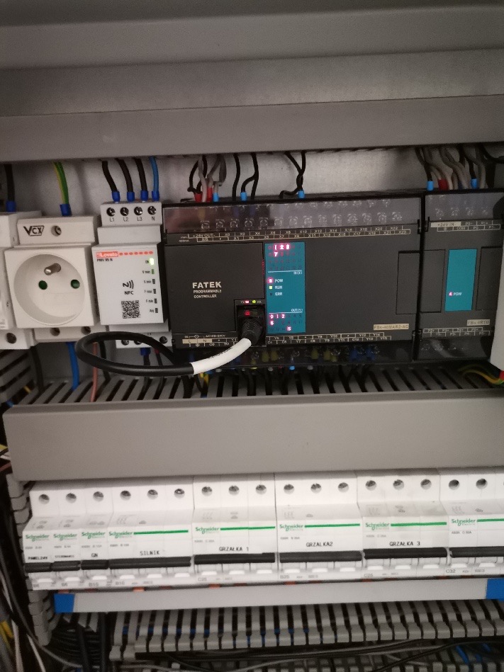 Rozdzielnica elektryczna z programowalnym sterownikiem FATEK, gniazdem sieciowym, modułem NFC i zabezpieczeniami Schneider Electric. Widoczne okablowanie i diody sygnalizacyjne.