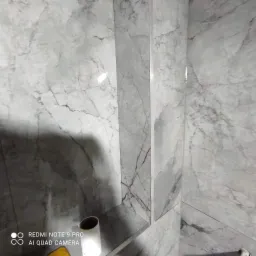 Wykończona ściana łazienki z szarymi płytkami imitującymi marmur, z wbudowaną półką i widoczną rolką papieru toaletowego.