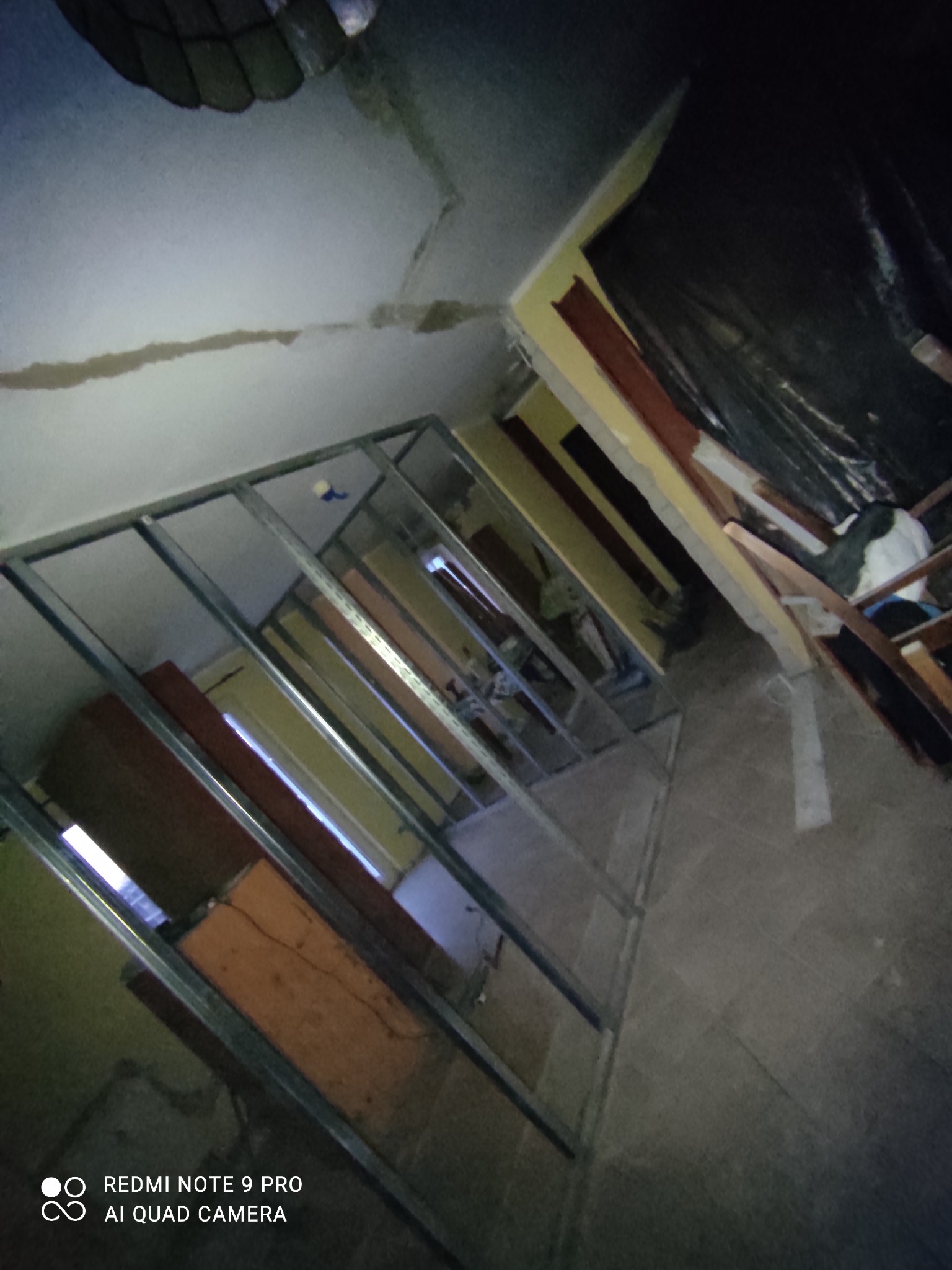 Montaż metalowego stelażu pod płytę karton-gips w trakcie prac wykończeniowych w pomieszczeniu z widocznymi śladami wcześniejszych prac na suficie i podłodze.