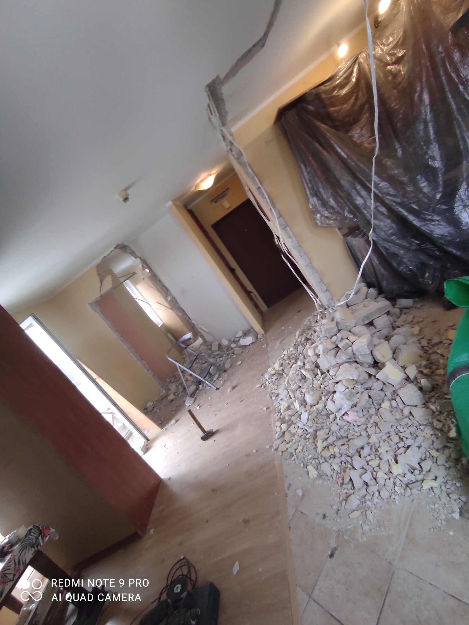 Wnętrze mieszkania w trakcie demontażu ściany, widoczny gruz, zabezpieczona folią strefa, narzędzia i drabina.