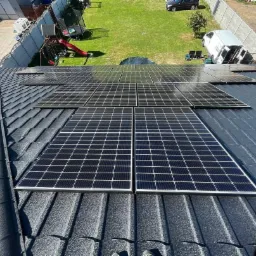 Panele słoneczne zamontowane na dachu z blachodachówki w słoneczny dzień, widok z góry na instalację i otoczenie domu.