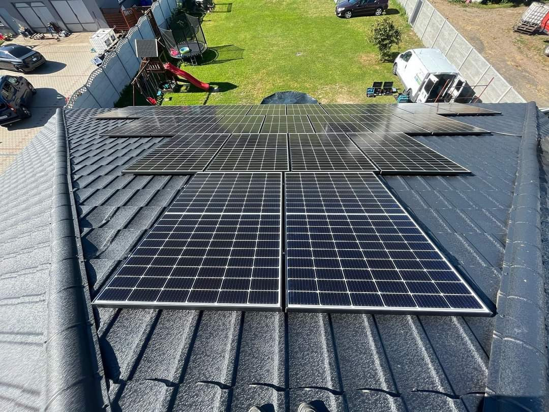 Panele słoneczne zamontowane na dachu z blachodachówki w słoneczny dzień, widok z góry na instalację i otoczenie domu.