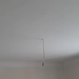 Gładki, biały sufit w trakcie prac wykończeniowych, z wystającym przewodem elektrycznym i widocznym fragmentem okna w rogu pomieszczenia.