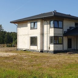 OknaGK - OKNOPLAST Góra Kalwaria - Surowy dom jednorodzinny w trakcie budowy, z zamontowanymi grafitowymi oknami i bramą garażową, widok z zewnątrz na działce.