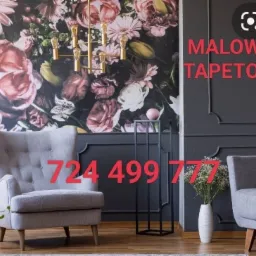 Elegancki pokój z szarą ścianą z dekoracyjnymi sztukateriami, fotel w stylu retro i tapeta w kwiaty, oświetlony złotym żyrandolem.