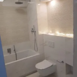 Wykończona łazienka w jasnych barwach z wanną, toaletą podwieszaną i deszczownicą, ściany wyłożone płytkami imitującymi marmur z poziomymi żłobieniami, oświetlenie punktowe i dekoracyjne lampki.