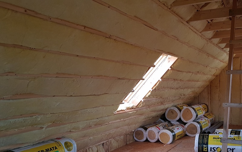 Poddasze ocieplone wełną mineralną, widoczne pakiety wełny Isover Super-Mata A32, okno dachowe w skosie dachu.