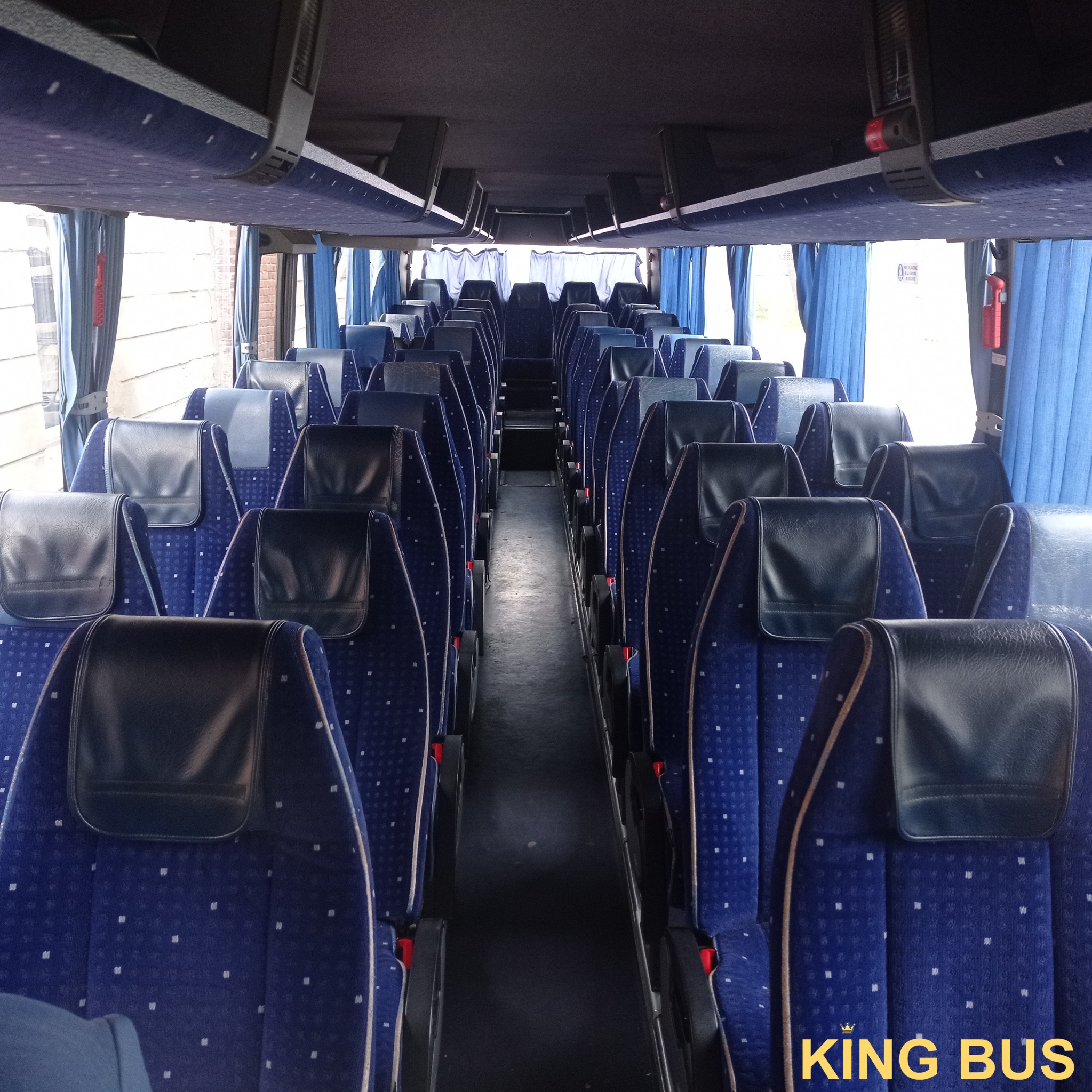 Wnętrze autobusu z rzędami niebieskich foteli z zagłówkami, widok z przodu kabiny wzdłuż przejścia.