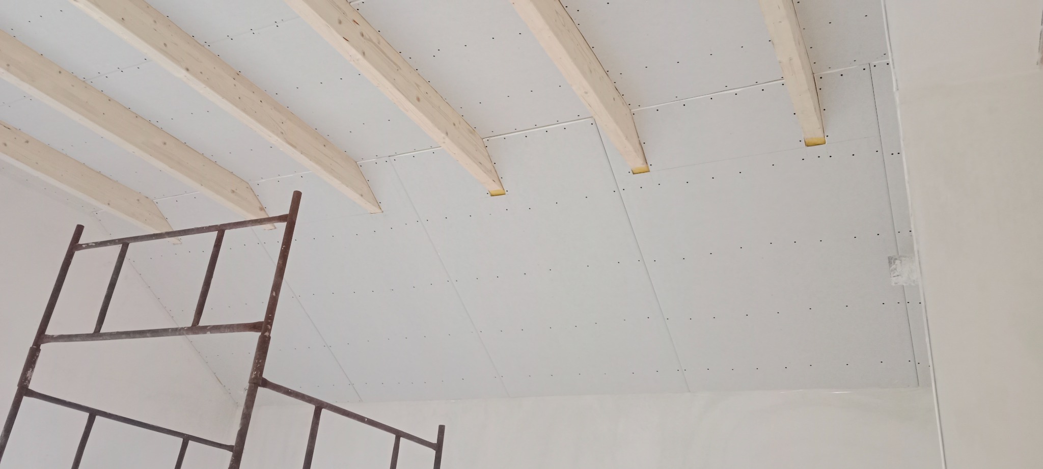 Montaż płyt karton gips na drewnianym stropie poddasza, widoczne rusztowanie i wkręty mocujące płyty.