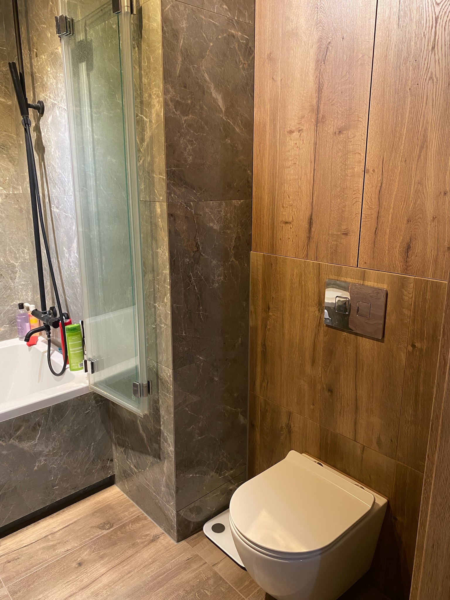 Nowoczesna aranżacja łazienki we Wrocławiu z kabiną prysznicową z czarną armaturą, wanną, podwieszaną toaletą i drewnopodobną okładziną ścienną.