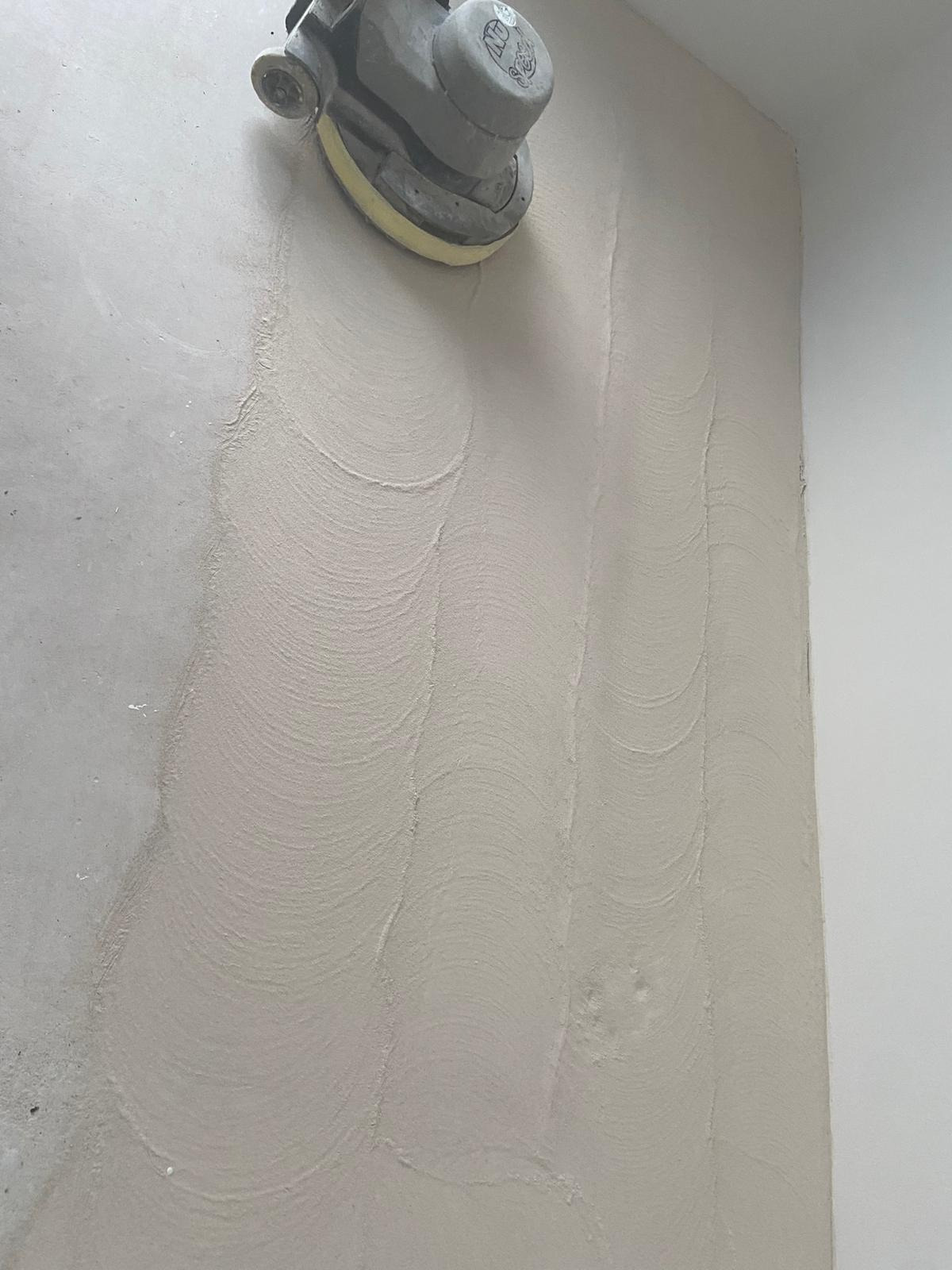 Szlifowanie ściany gipsowej szlifierką oscylacyjną, widoczne ślady po szlifowaniu w kształcie półokręgów.