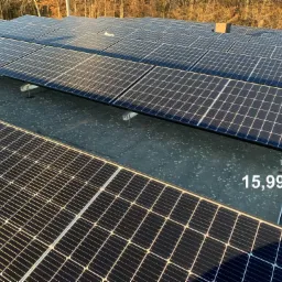 Instalacja fotowoltaiczna o mocy 15,99 kW na płaskim dachu pokrytym papą, widok z góry, w tle drzewa.