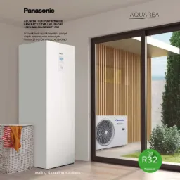 Biała, kompaktowa pompa ciepła Panasonic Aquarea, model all-in-one, umieszczona w jasnym pomieszczeniu. Na zewnątrz, za oknem widoczny zewnętrzny moduł pompy ciepła i zielony ogród. W rogu kosz...