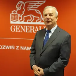 Mężczyzna w garniturze na tle pomarańczowej ściany z logo firmy ubezpieczeniowej Generali.