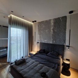 Ferbel - Nowoczesna sypialnia z łóżkiem w odcieniach szarości, geometryczną tapetą za wezgłowiem i odbiciem pokoju w lustrzanej ścianie, z minimalistycznym oświetleniem punktowym i zasłonami.