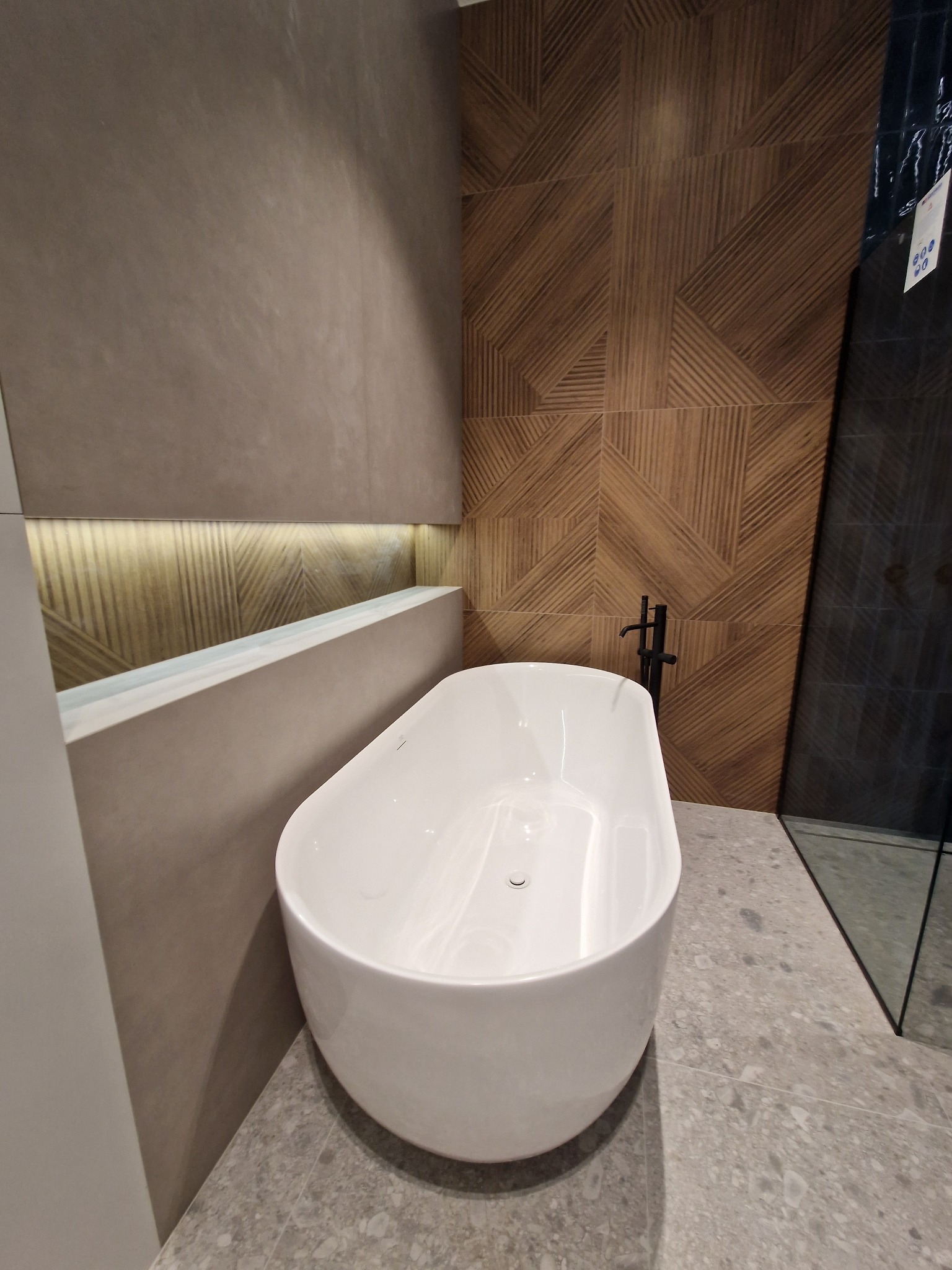 Nowoczesna, wolnostojąca wanna w łazience z dekoracyjną, drewnopodobną ścianą i szarą, kamienną podłogą.