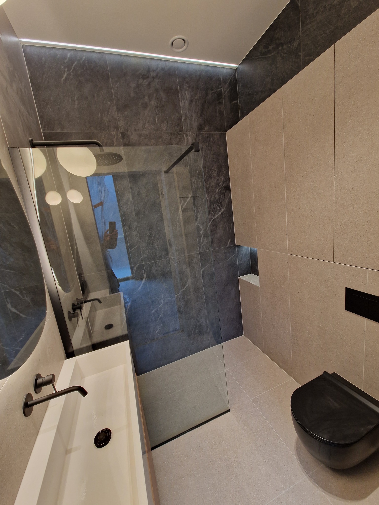 Nowoczesna łazienka z kabiną prysznicową typu walk-in, umywalką nablatową, armaturą w kolorze czarnym i podświetleniem LED podsufitowym.