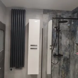 Nowoczesna łazienka z kabiną prysznicową typu walk-in, grzejnikiem żeberkowym w kolorze antracytowym, wiszącą białą szafką i płytkami imitującymi marmur w odcieniach szarości i błękitu.