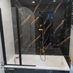 Nowoczesna łazienka z czarno-złotymi płytkami imitującymi marmur, białą wanną i czarną armaturą oraz grzejnikiem drabinkowym, szklany parawan nawannowy z czarnymi profilami.