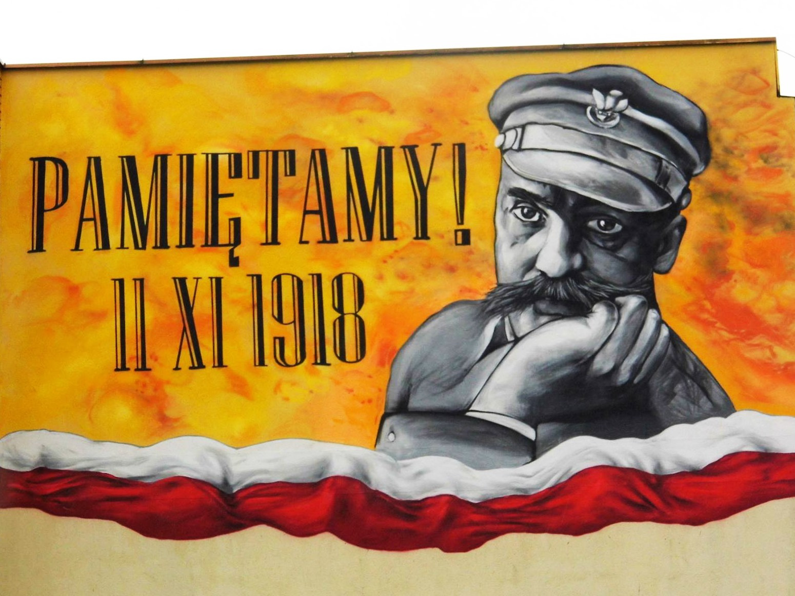 Mural na ścianie budynku z portretem Józefa Piłsudskiego, datą 11 XI 1918 i napisem 'Pamiętamy!', stylizowany na flagę Polski w dolnej części.