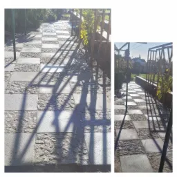 Ścieżka z kostki granitowej ułożona w szachownicę, z widocznymi cieniami drewnianej konstrukcji i zielenią w tle.