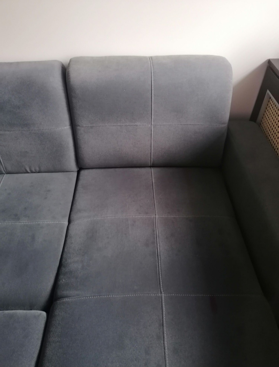 Fragment szarej, modułowej sofy z widocznymi szwami i subtelną teksturą materiału, ustawionej na tle jasnej ściany.