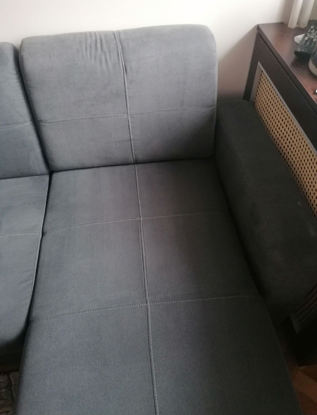 Szara sofa z wyraźnymi przeszyciami, widok z góry, obok szafka z ażurową wstawką.