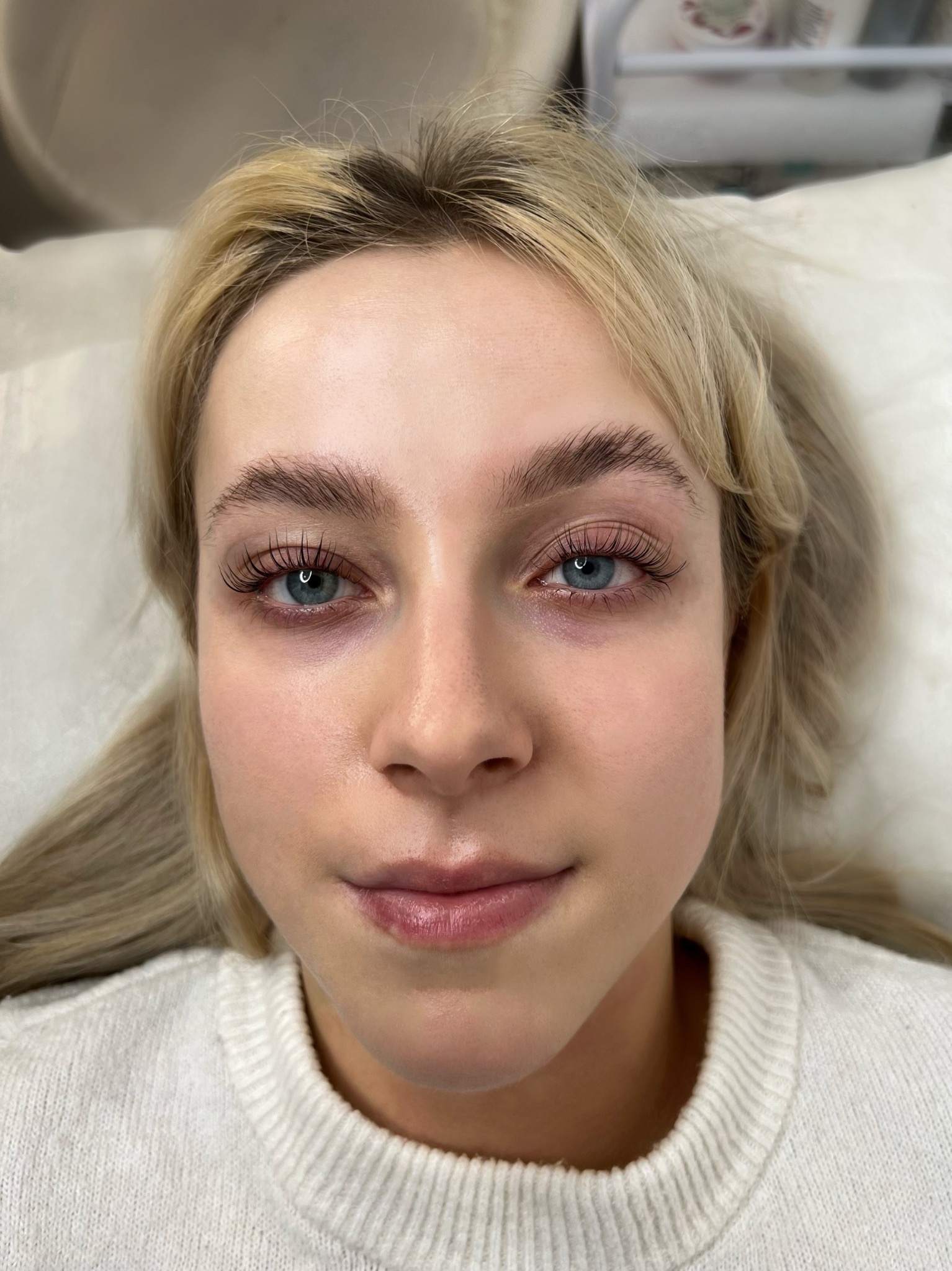 Twarz młodej kobiety z delikatnym makijażem permanentnym brwi i świeżo przedłużonymi rzęsami, widoczna z bliska w ujęciu z góry.