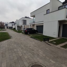 DEVELOPMENT ANDRII HULYCH - Rząd nowoczesnych, białych domów jednorodzinnych z szarymi garażami i czarnym samochodem osobowym zaparkowanym przed jednym z nich, widok z brukowanej drogi dojazdowej.