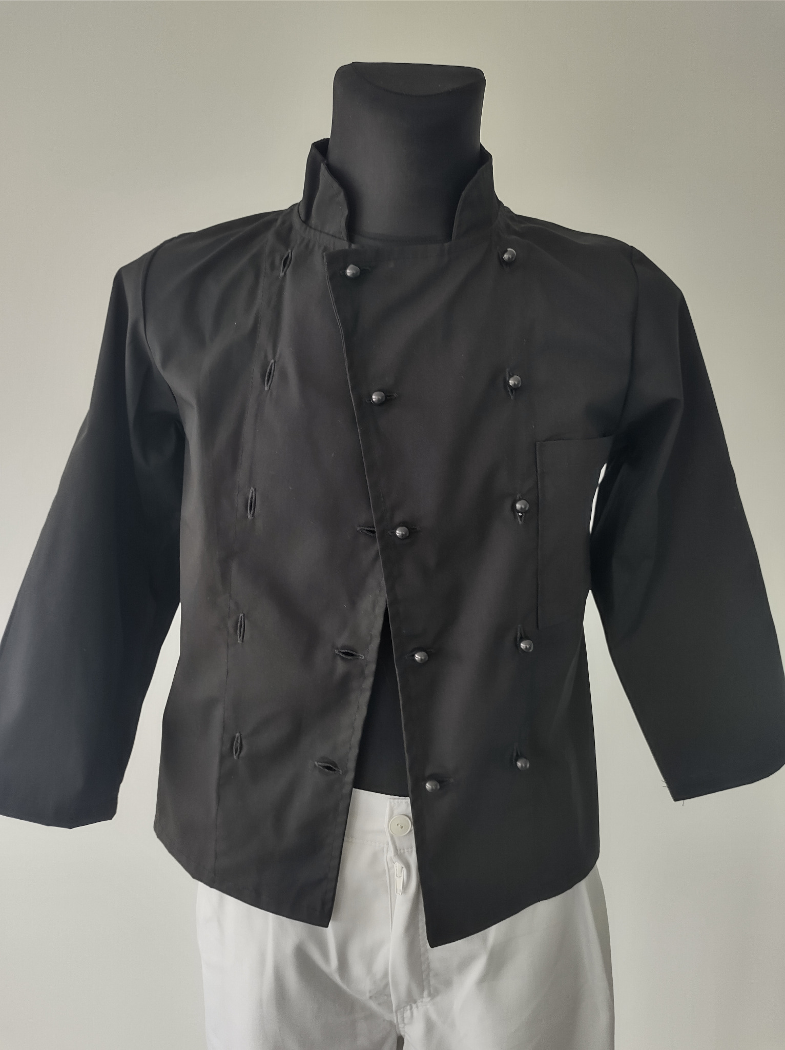 Czarna bluza kucharska z guzikami na manekinie, widoczne białe spodnie, neutralne tło.