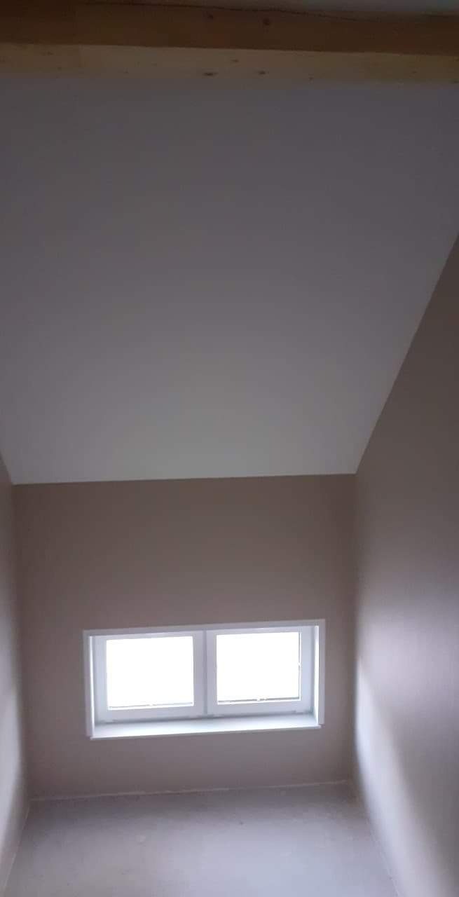 Poddasze po remoncie: skośny sufit pomalowany na biało, ściany w odcieniach beżu, okno PCV z dwoma skrzydłami.