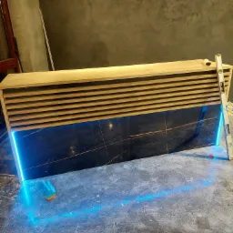 Nowoczesna zabudowa z drewnianymi lamelami i podświetlanymi płytami z efektem marmuru, poziomica oparta o ścianę, widoczny fragment podłogi i ściany z surowym wykończeniem.