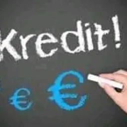 Napis 'Kredit!' wykonany białą kredą na czarnej tablicy obok symboli euro, z których jeden jest niebieski, a dłoń trzyma kredę gotową do pisania.