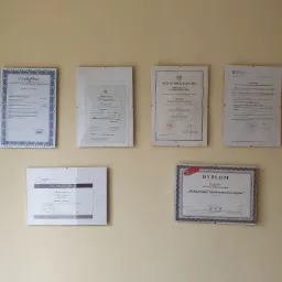 Ściana z powieszonymi certyfikatami, dyplomami i zaświadczeniami, w tym dyplom detektywistyczny zaawansowany oraz akt mianowania na stopień policyjny.