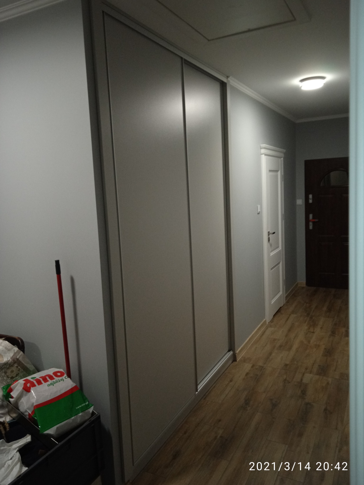 Długa szafa wnękowa z przesuwnymi drzwiami w korytarzu, widoczna torba na zakupy Dino i mop oparty o ścianę.