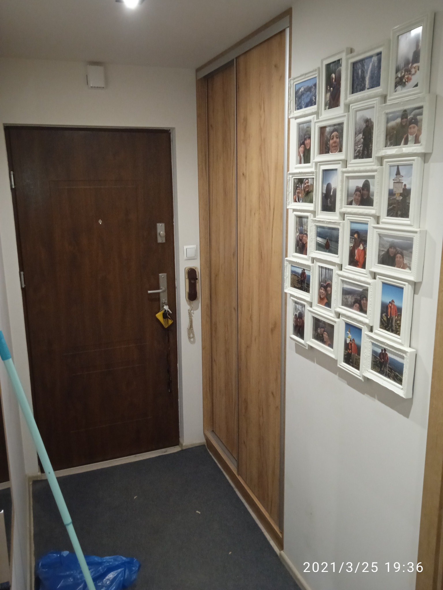 Korytarz z drewnianą szafą przesuwną, brązowymi drzwiami wejściowymi i galerią białych ramek ze zdjęciami na ścianie.