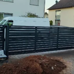 Nowoczesna, przesuwna brama z poziomych, metalowych profili, z automatyką, widoczna sterta ziemi po montażu, na tle dwóch domów i białego samochodu dostawczego.