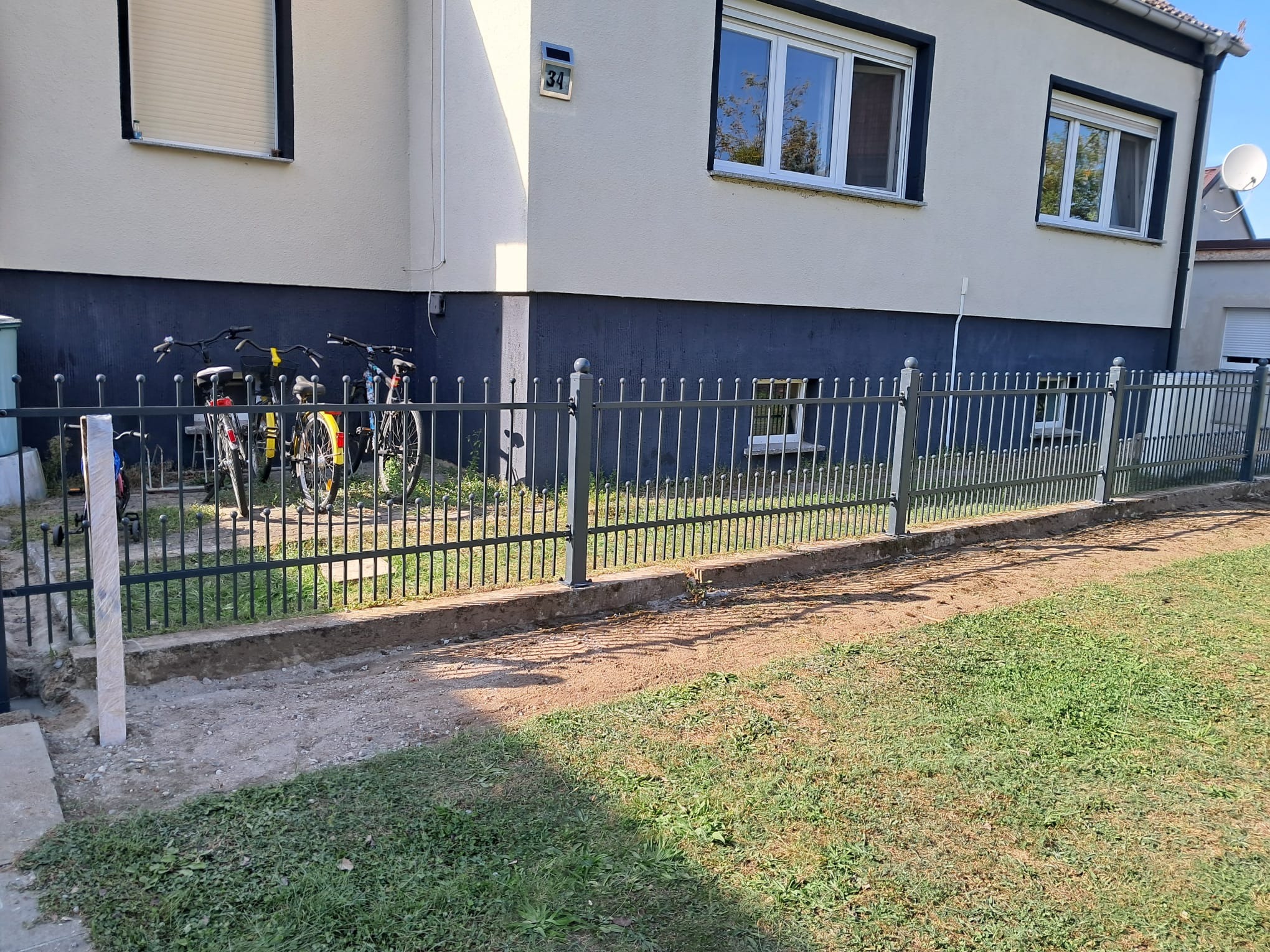 Fragment nowo postawionego, czarnego ogrodzenia metalowego przed budynkiem z numerem 34, widoczne rowery opierające się o ogrodzenie.