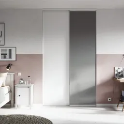 Nowoczesna sypialnia z łóżkiem, stolikiem nocnym, biurkiem i przesuwnymi drzwiami szafy, udekorowana galerią plakatów w czarnych ramkach na ścianie pomalowanej w dwóch odcieniach różu i bieli.