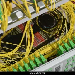 Panel krosowniczy z uporządkowanymi żółtymi kablami światłowodowymi i zielonymi złączami, widoczne elementy w kolorze czerwonym i czarnym, z metalową obudową.