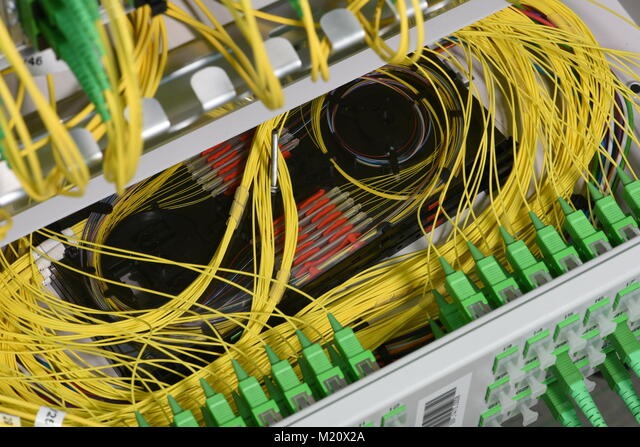 Panel krosowniczy z uporządkowanymi żółtymi kablami światłowodowymi i zielonymi złączami, widoczne elementy w kolorze czerwonym i czarnym, z metalową obudową.