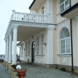 Elegancki dom z beżową elewacją, kolumnami i balkonem, wykończony kostką granitową ułożoną we wzór koncentrycznych okręgów.