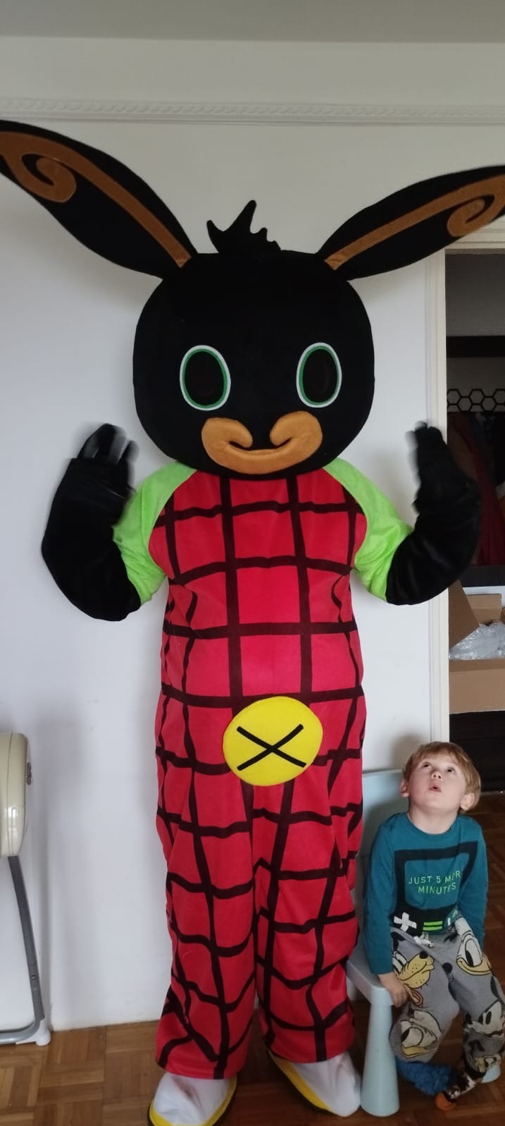 Osoba w kostiumie królika Bing stoi obok chłopca siedzącego na krześle, który patrzy w górę.