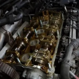 Otwarta głowica silnika samochodowego z widocznymi wałkami rozrządu, śladami oleju i elementami mocującymi, podczas serwisu.