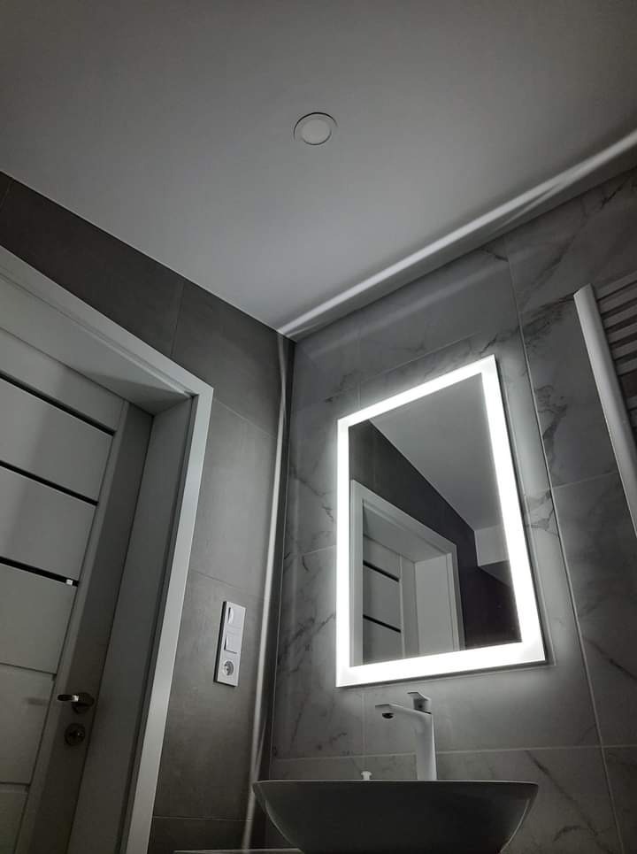 Nowoczesna łazienka z szarymi płytkami imitującymi marmur, podświetlanym lustrem LED i minimalistyczną umywalką nablatową.