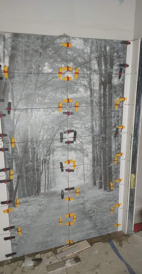 Układanie płytek z motywem zimowego lasu na ścianie, z użyciem systemu poziomowania płytek (klipsy i kliny).