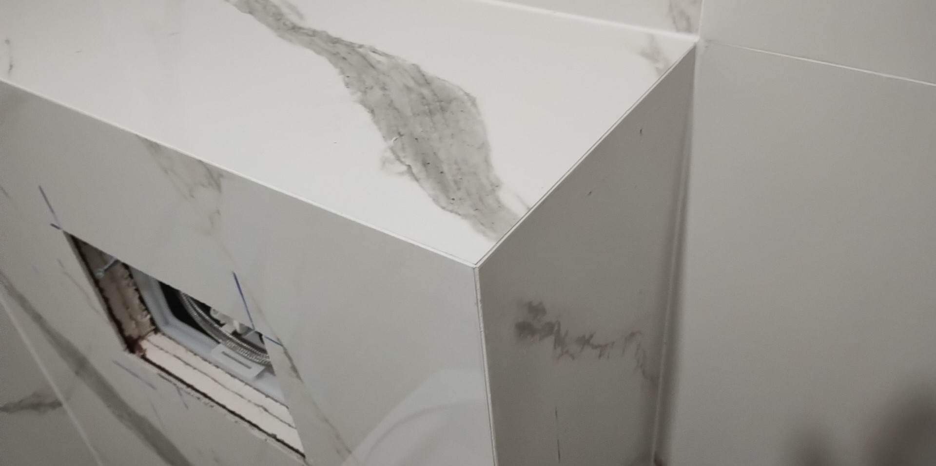 Fragment zabudowy geberitu z białych płytek imitujących marmur, z widocznym otworem rewizyjnym w trakcie montażu.