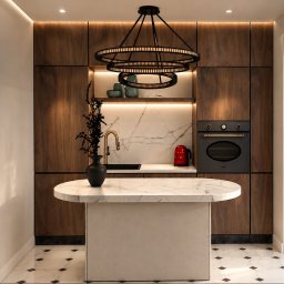 Hort Studio - Elegancka kuchnia z ciemnymi szafkami z orzecha, marmurową wyspą i blatem, złotą baterią, czarnym piekarnikiem Smeg i czerwonym czajnikiem. Centralnie zawieszony czarny żyrandol.