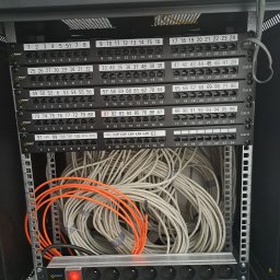 IPINSTAL Usługi Elektryczne Paweł Świstek - Panel krosowniczy z podłączonymi kablami sieciowymi, widoczny również przedłużacz z czerwonym włącznikiem w szafie rack.