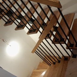 Pol-welder - Drewniane schody z czarnymi, metalowymi balustradami, widziane z góry pod kątem. Jasne drewno stopni kontrastuje z ciemnymi elementami konstrukcyjnymi.